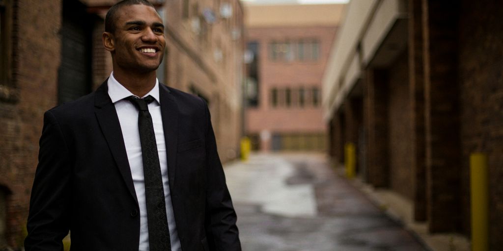 smiling man standing between brown concrete buildings at daytime